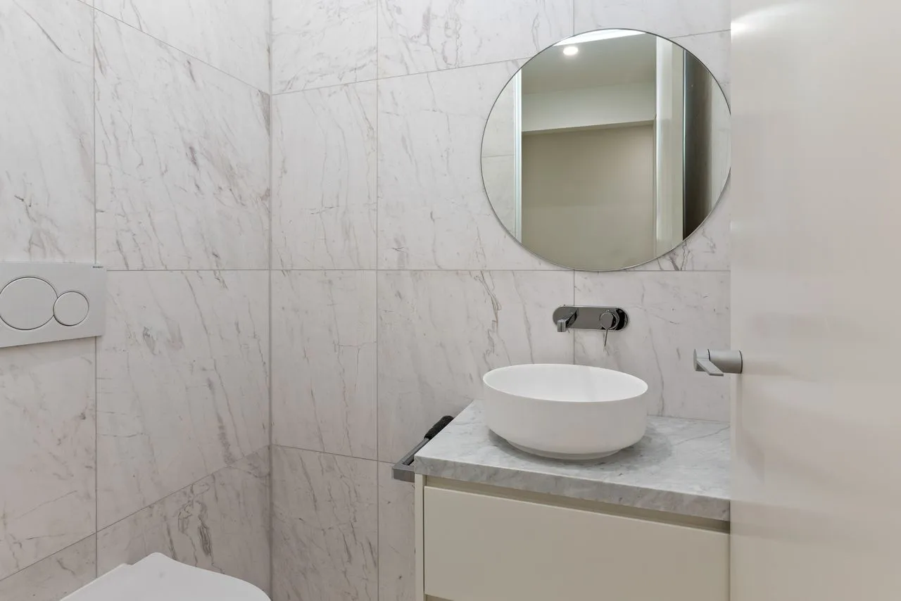 Un baño revestido de azulejos con un lavabo redondo y un espejo circular.