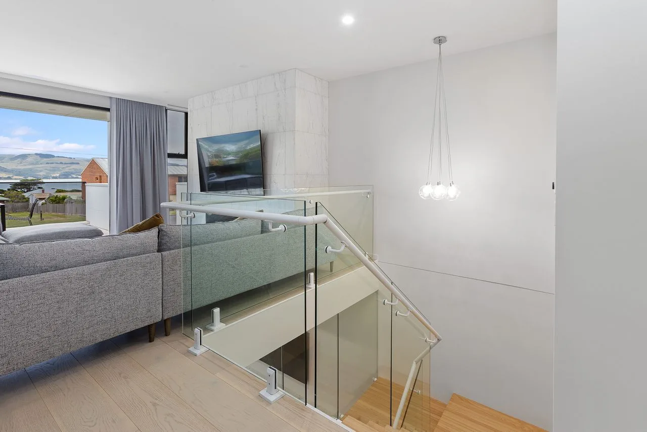 Una luminosa sala de estar da a una escalera con barandilla de vidrio y una vista por la ventana.