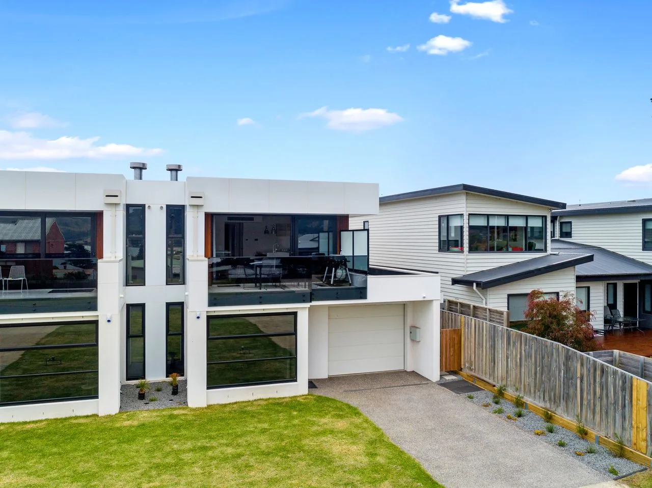 Exterior de una casa moderna con grandes ventanas, césped y entrada para vehículos.