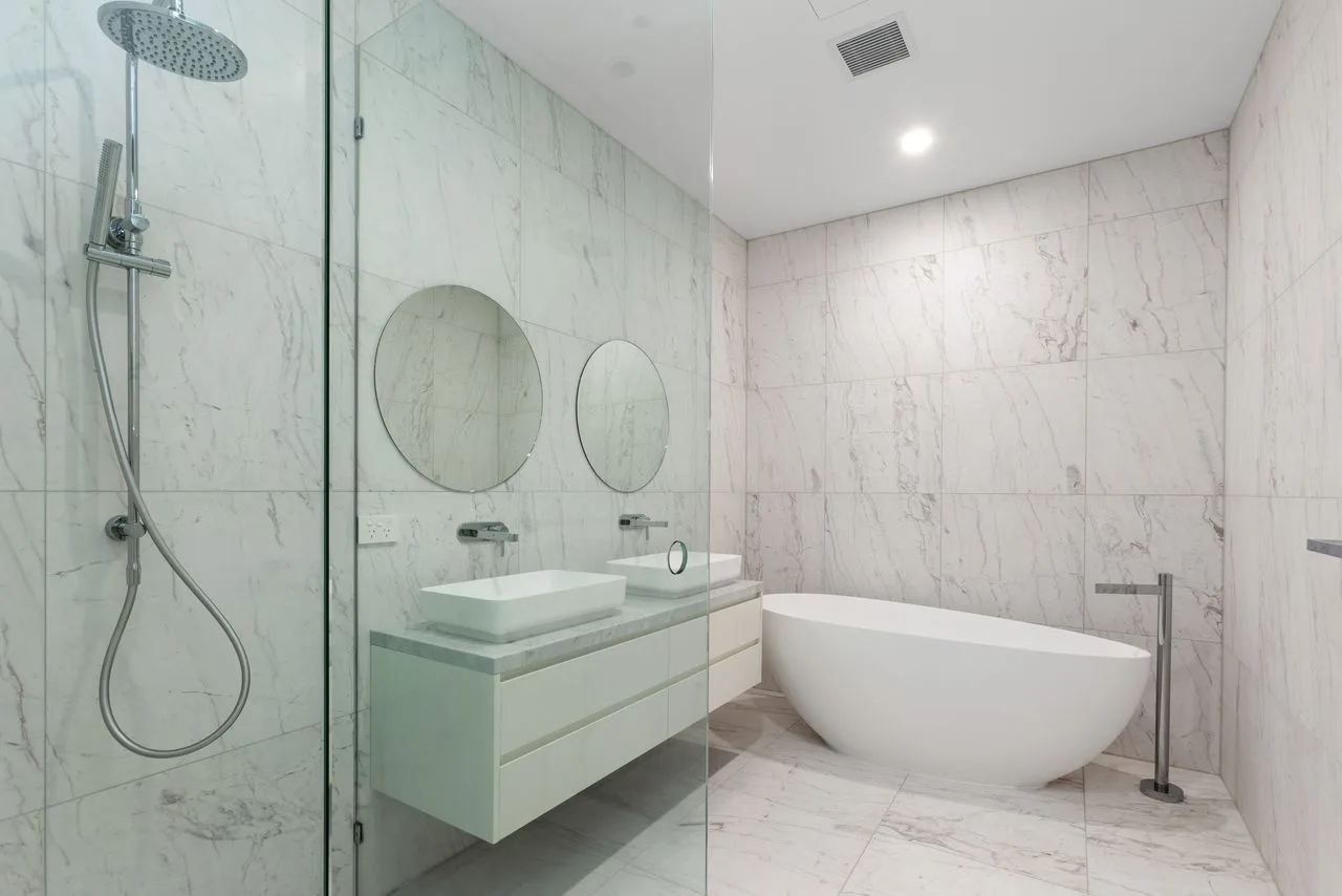 A bright marble bathroom with a glass-enclosed shower and freestanding bathtub.
