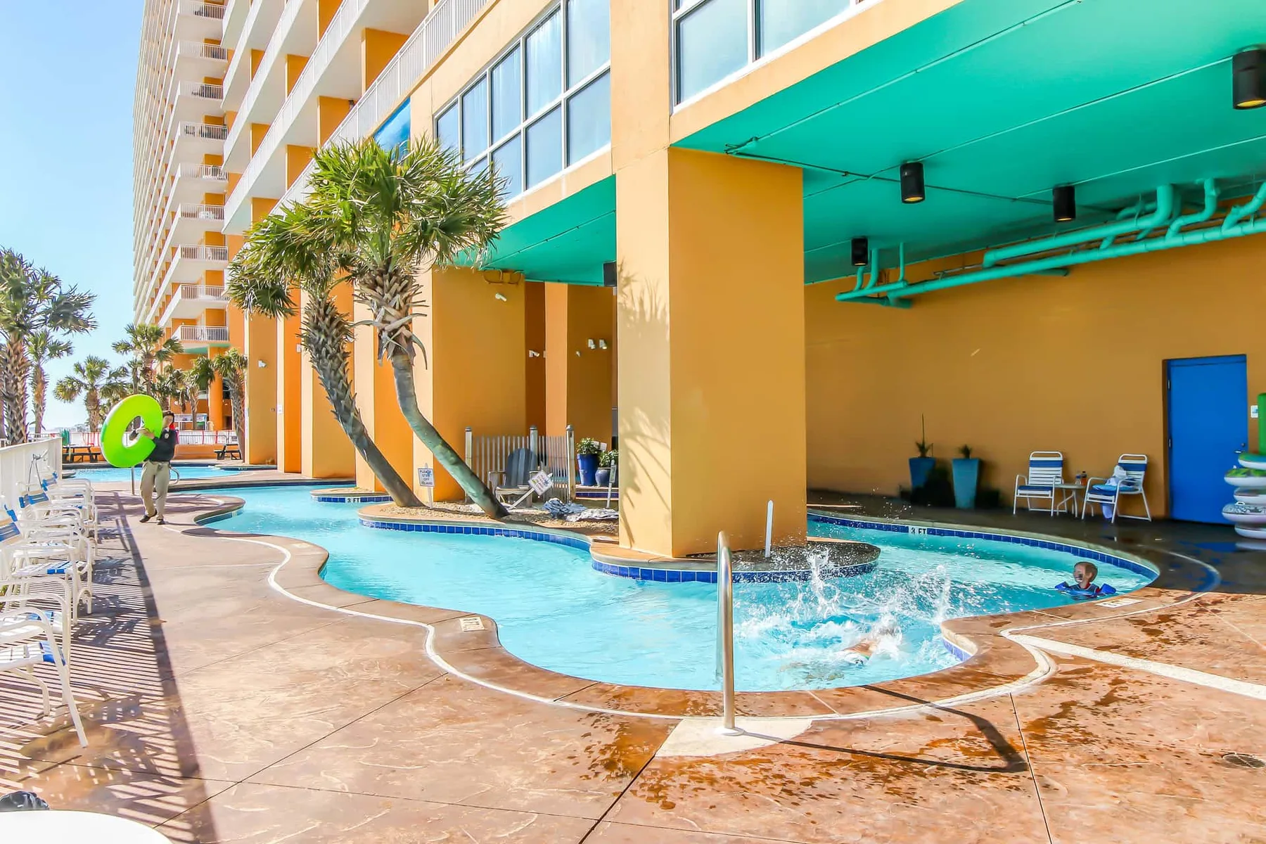 Una piscina al aire libre bordea un edificio de colores vivos, con tumbonas alrededor.