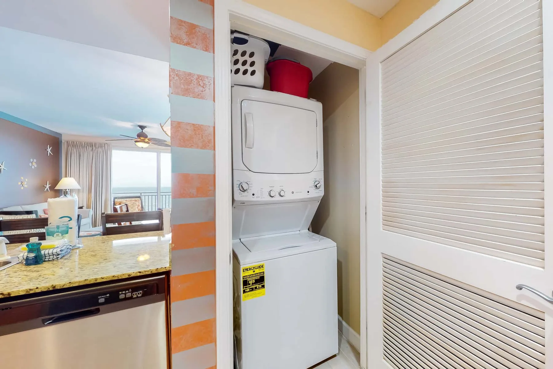 Área de lavado con lavadora y secadora apiladas junto a una encimera de cocina.