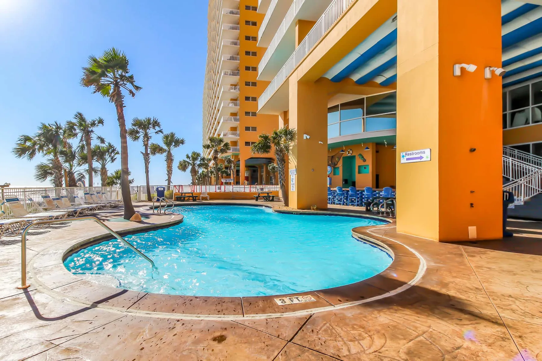 Una piscina exterior curva junto a un edificio colorido de varios pisos.
