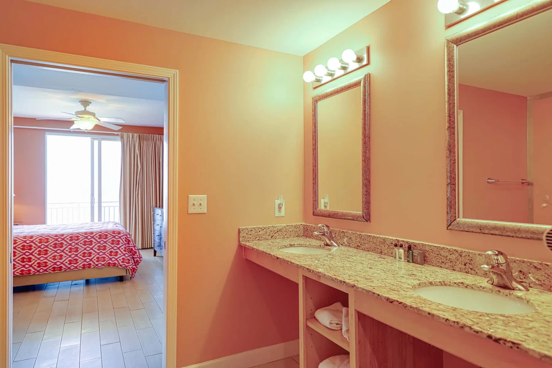Un tocador de baño con una encimera larga y espejos, junto a una puerta abierta.