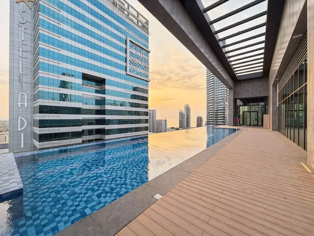 An elevated outdoor pool and wooden deck overlook a city skyline.