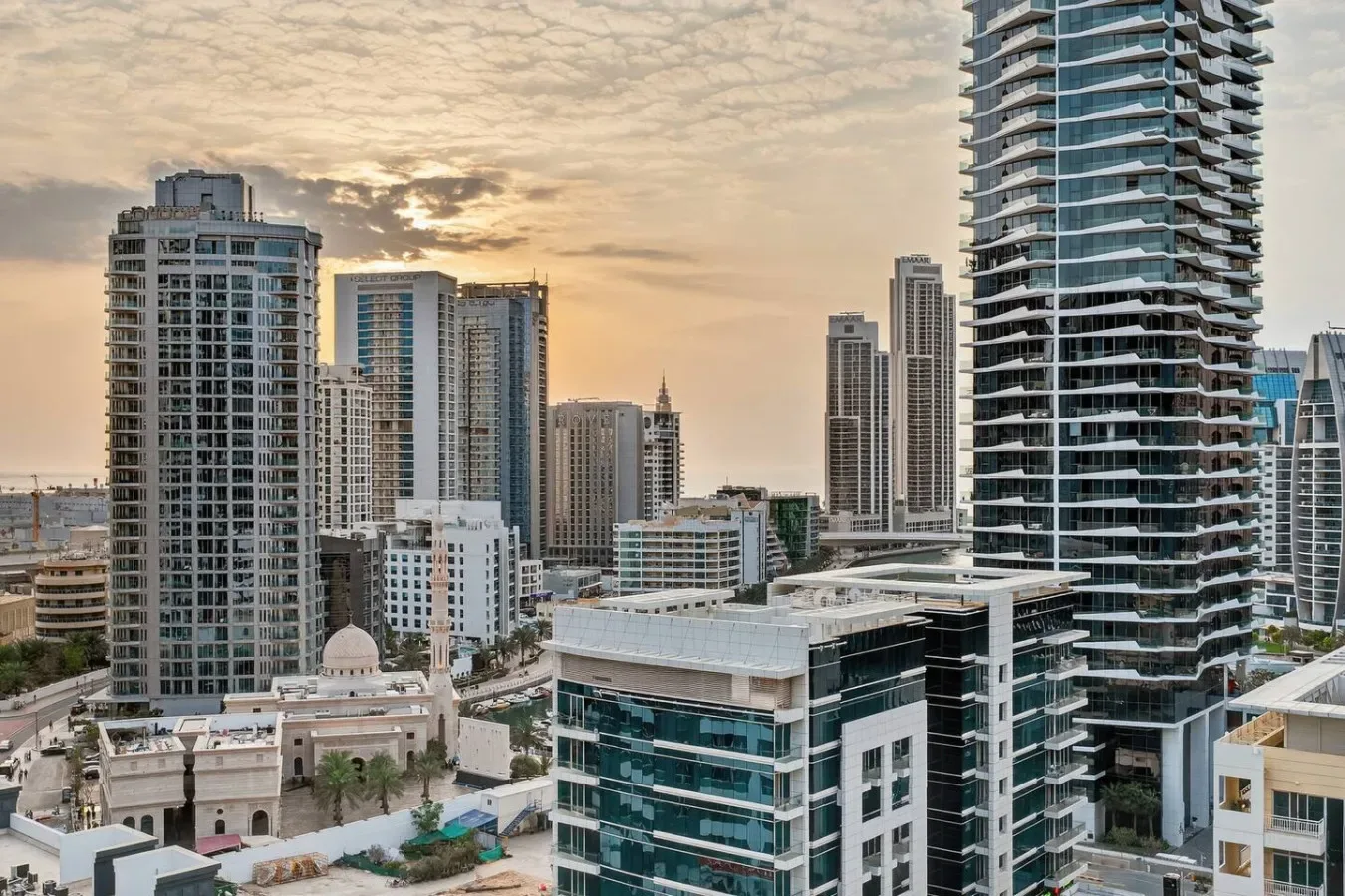 A city skyline of high-rise buildings beneath a cloudy sunset sky.