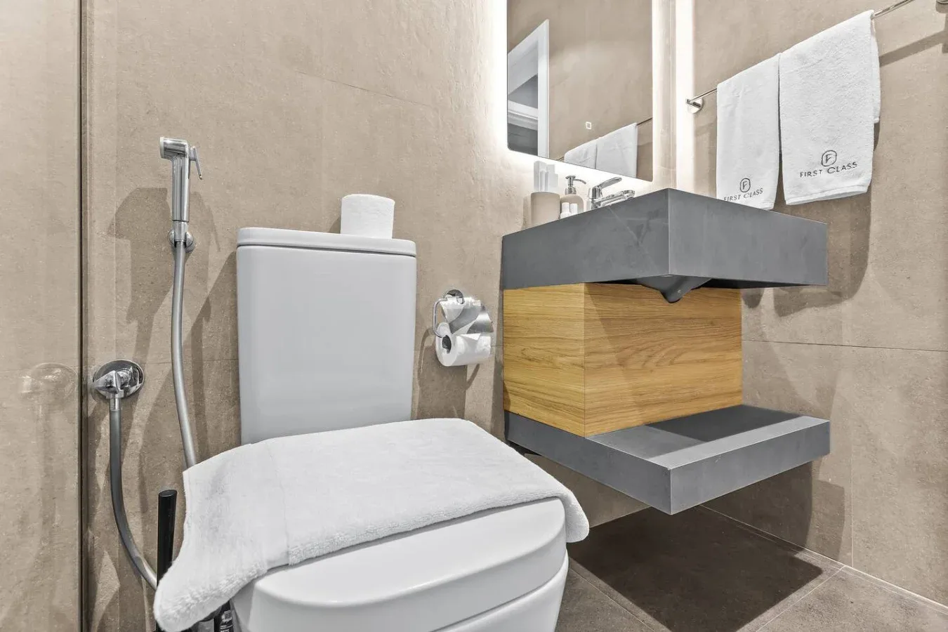 Un baño con inodoro, lavabo suspendido y toallas.