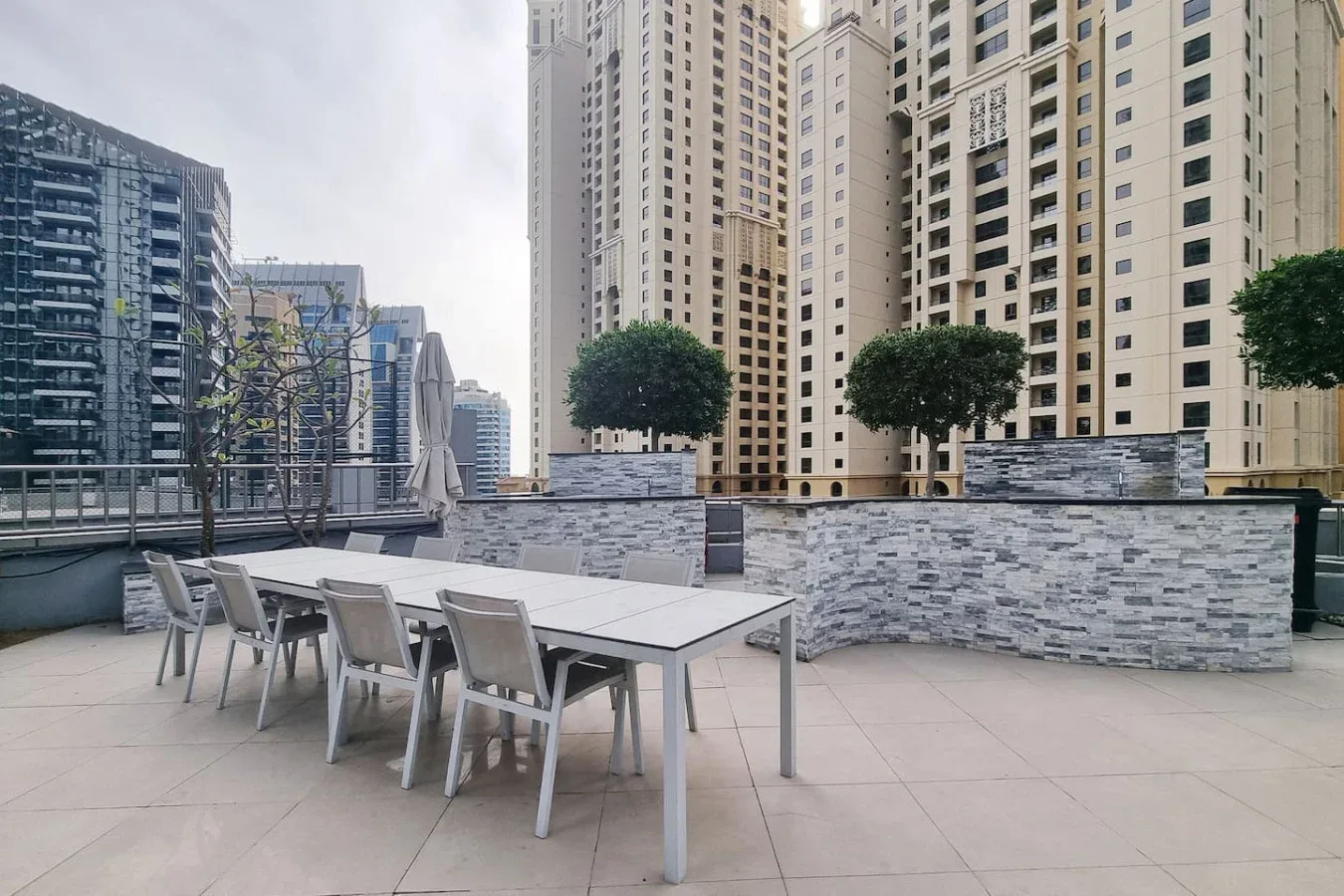 Una terraza exterior tiene una mesa larga con asientos junto a un muro bajo.