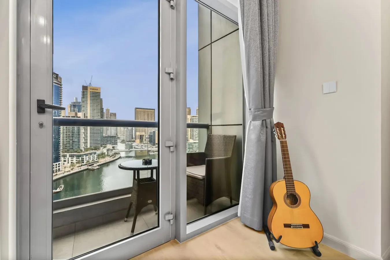 Una guitarra está junto a puertas de vidrio con vistas a una ciudad junto al agua.