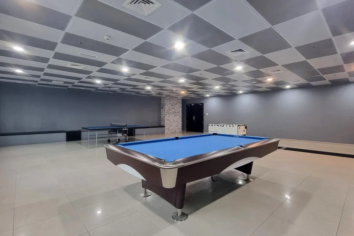 Una sala recreativa con una mesa de billar de paño azul y otras mesas al fondo.