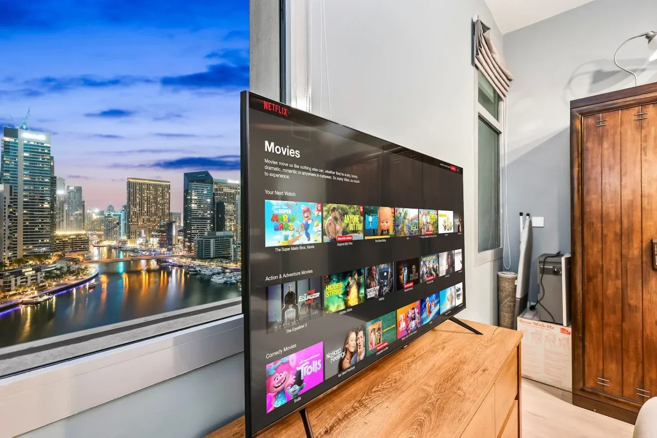 Un dormitorio con un televisor sobre un mueble de madera junto a una gran ventana con vistas a la ciudad.