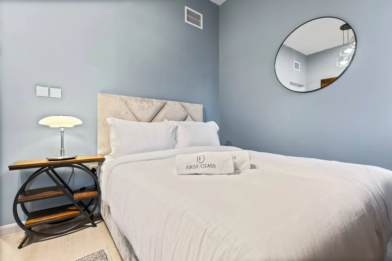 Un dormitorio con una cama bien arreglada y un espejo redondo en la pared.