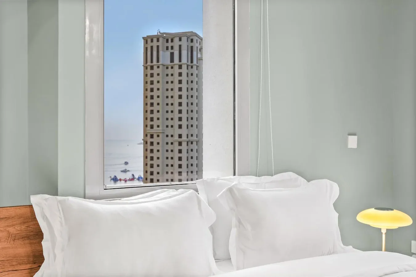 Un dormitorio con almohadas blancas junto a una ventana amplia con vistas a una torre cercana.