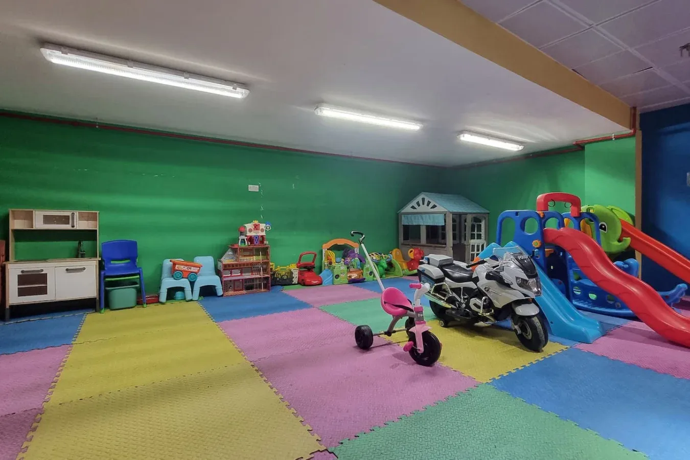 Una colorida sala de juegos interior con una estructura para trepar y juguetes sobre un suelo acolchado.