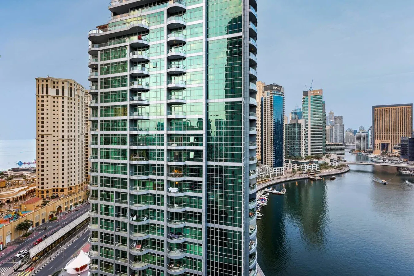 Un edificio alto de vidrio domina un canal junto al mar y edificios urbanos cercanos.