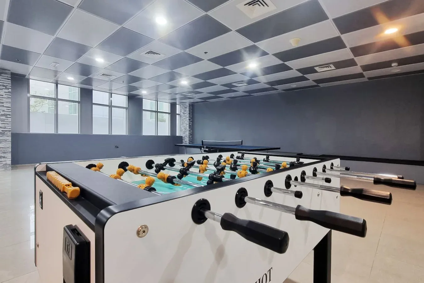 Una sala de futbolín con varias mesas bajo un techo de cuadros.