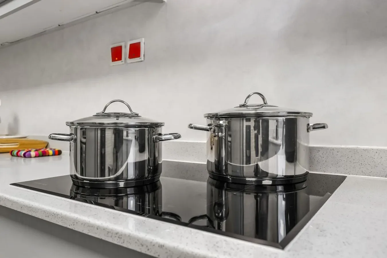 Una placa de cocina con dos ollas de acero inoxidable bajo un salpicadero claro.