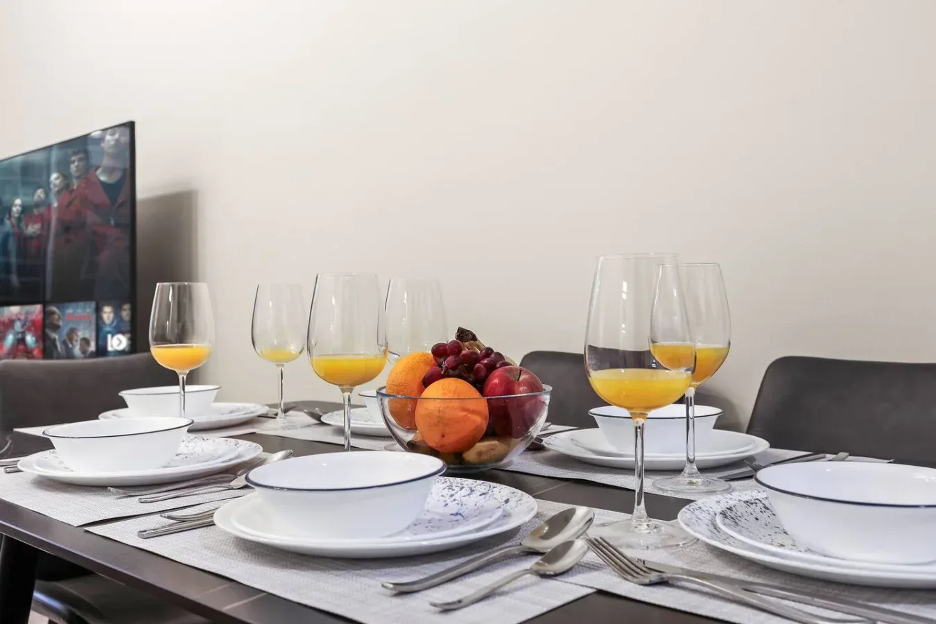 Una mesa de comedor está puesta con platos, copas y un cuenco de fruta.