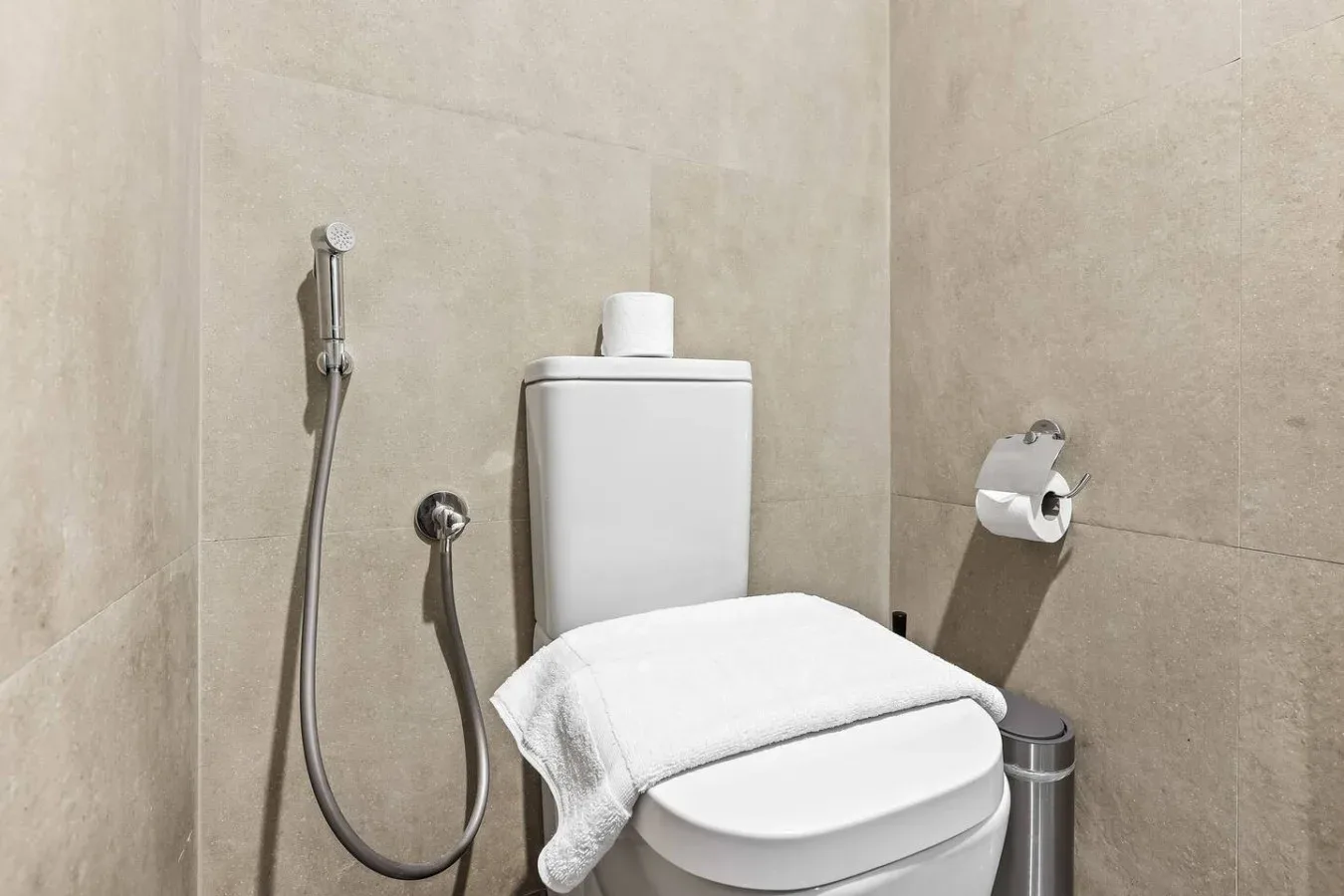 Un baño con azulejos, un inodoro y una ducha higiénica de mano.