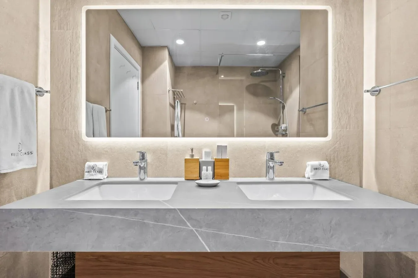 Un tocador de baño con dos lavabos está debajo de un gran espejo iluminado.