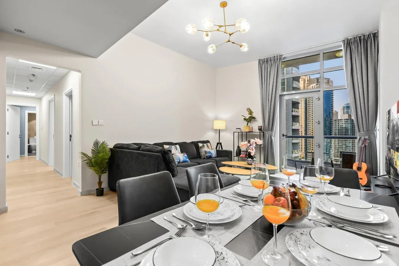 Comedor con la mesa puesta y una sala de estar junto a ventanales.
