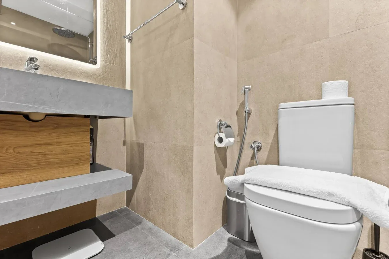 Un baño con inodoro, lavabo suspendido y paredes de azulejos beige.
