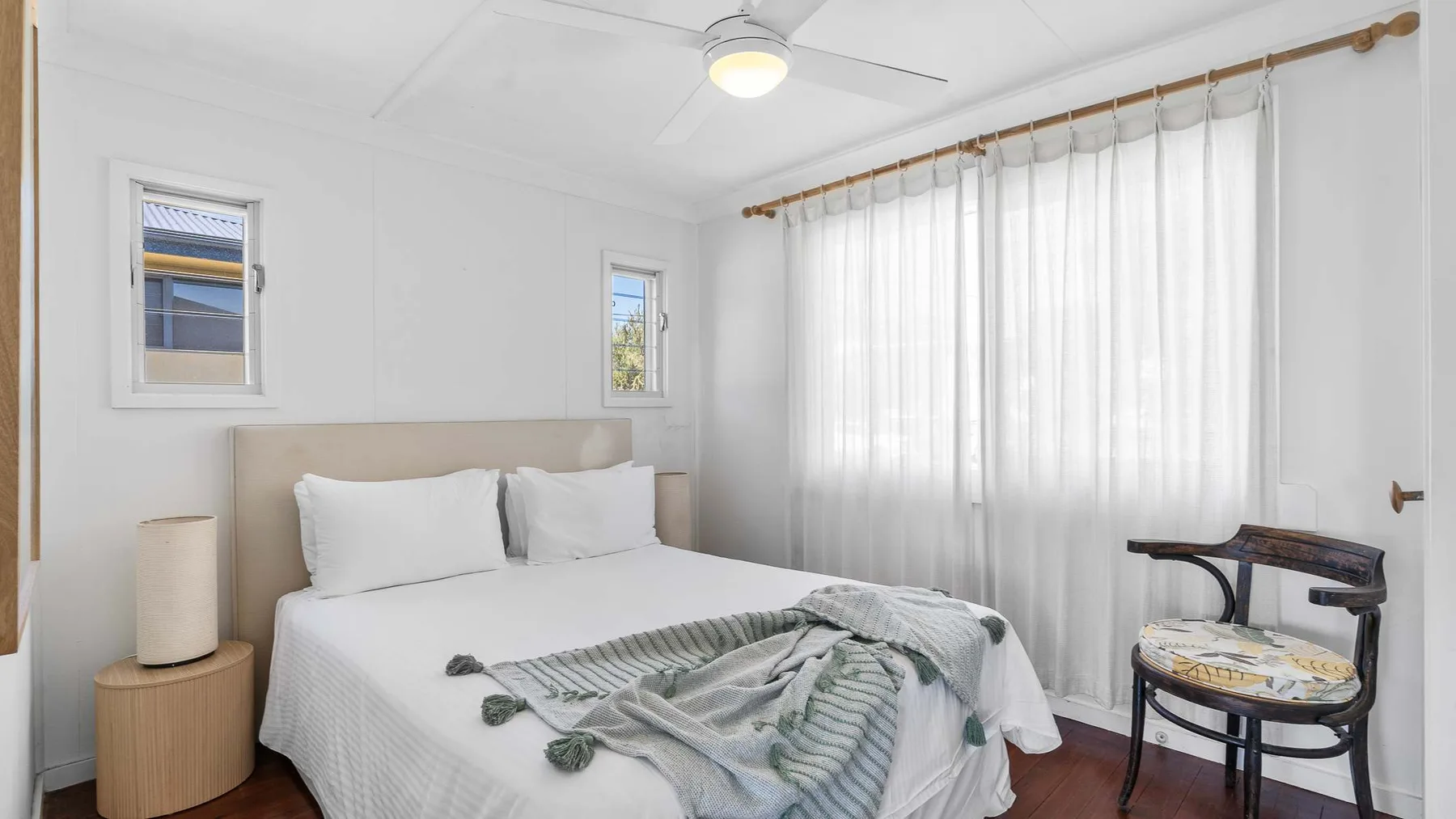 Un dormitorio con una cama bien tendida y cortinas translúcidas.