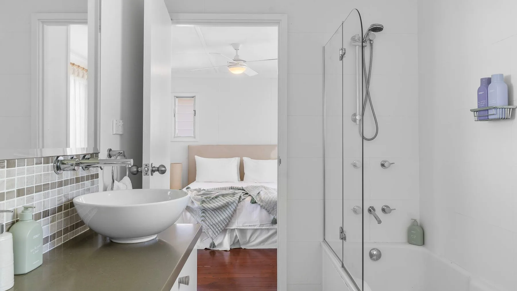 Un baño con lavabo y ducha, abierto hacia un dormitorio.