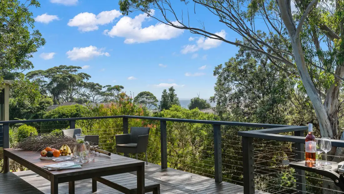 An outdoor dining deck overlooks leafy trees beneath a blue sky.