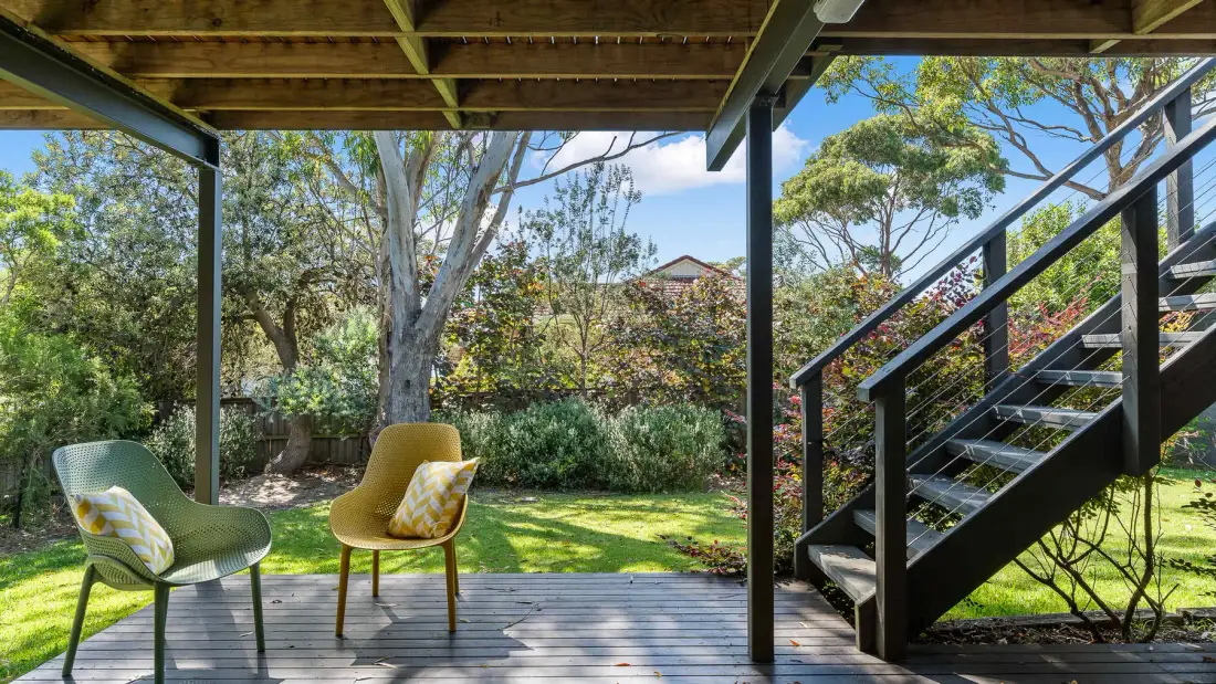 Una terraza exterior sombreada da a un jardín frondoso, con escaleras junto a los asientos.