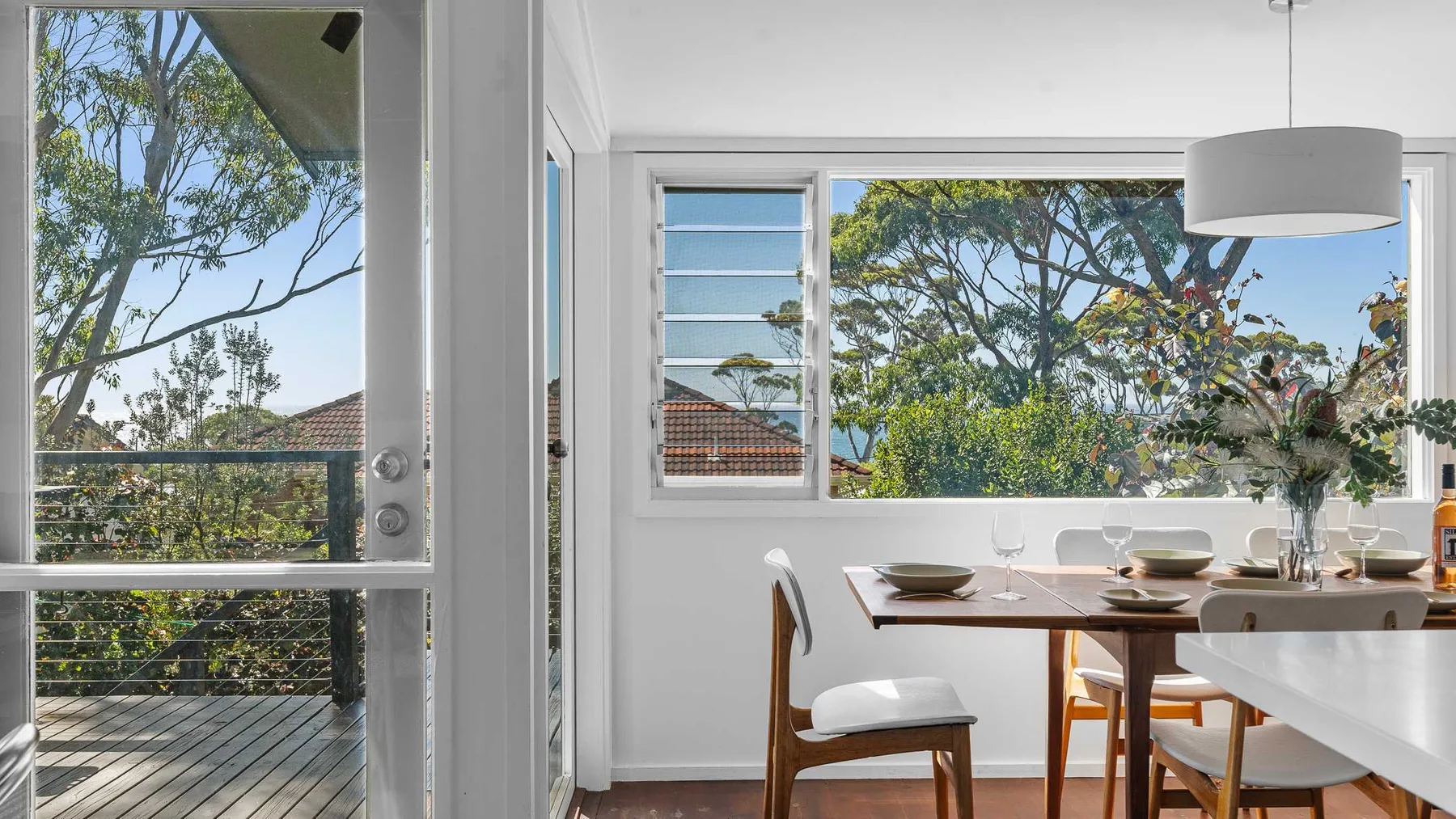 Un comedor luminoso da a un balcón, con árboles frondosos visibles por las ventanas.
