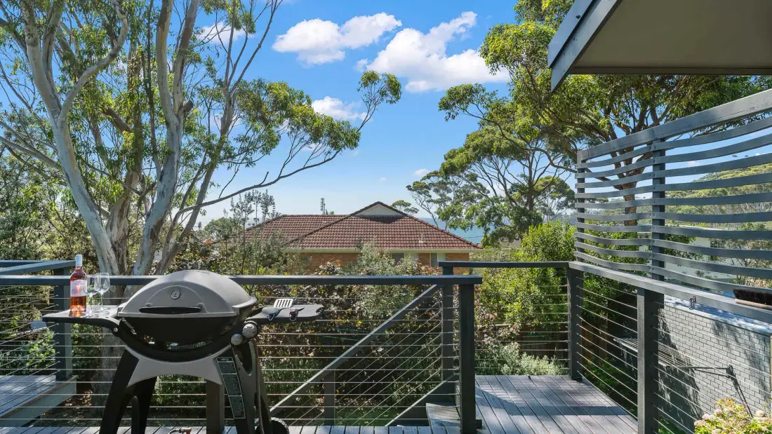 Una terraza exterior con una barbacoa y árboles frondosos al otro lado de la barandilla.