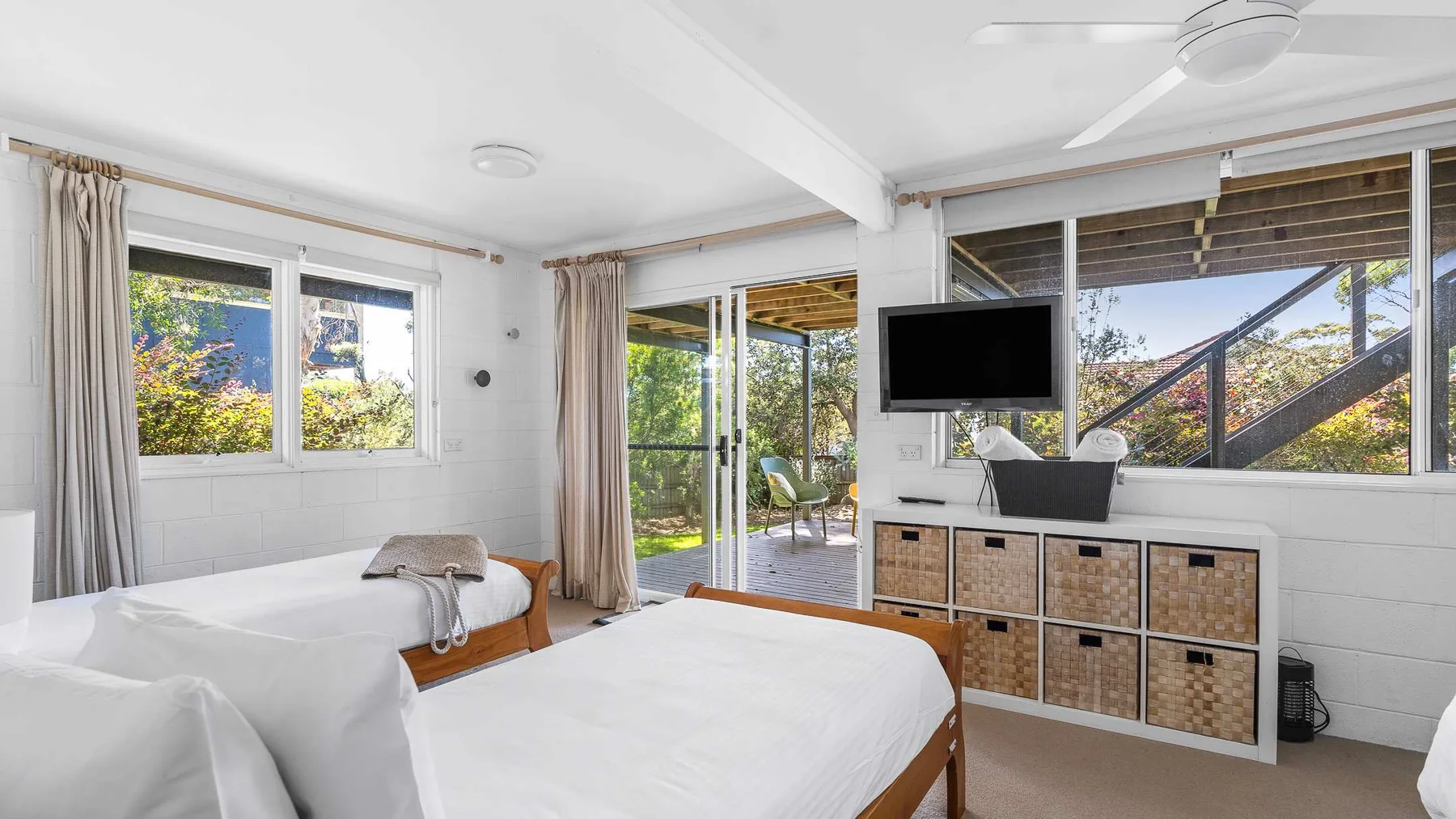 Un dormitorio luminoso con dos camas y un televisor junto a las ventanas.