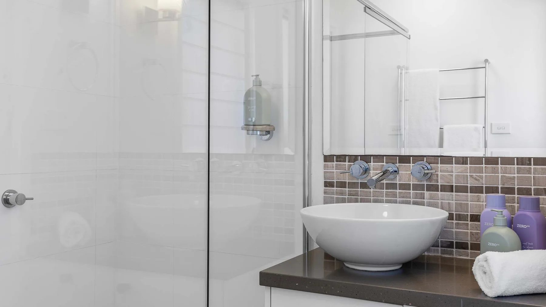 Un baño luminoso con lavabo sobre encimera y ducha de vidrio.