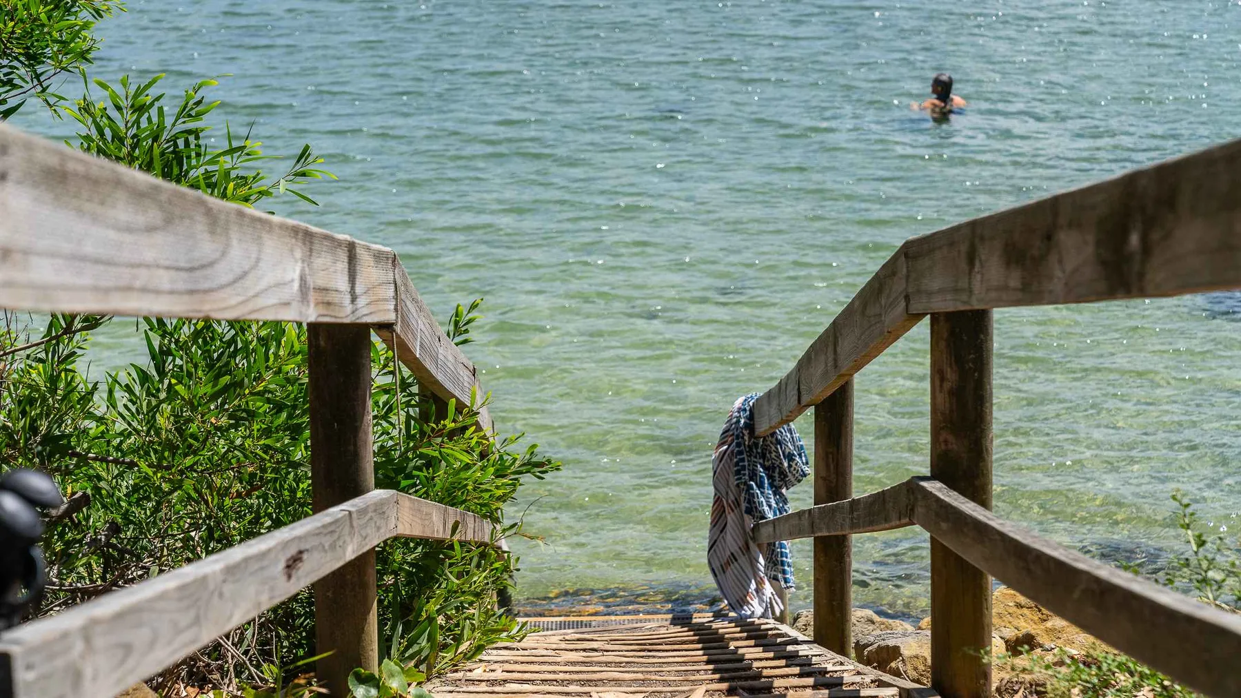 Unas escaleras de madera bajan hasta el agua, donde se ve una persona nadando.