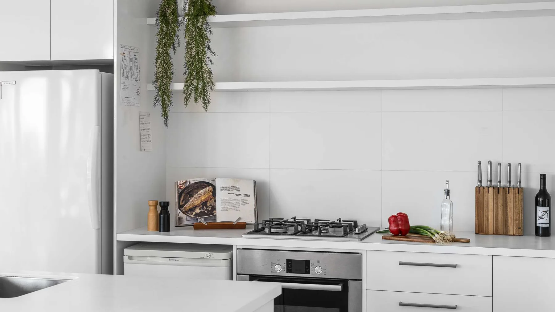Una cocina moderna con armarios blancos, un refrigerador y una placa de cocina.