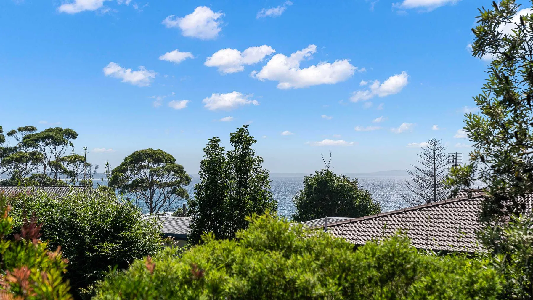 A coastal scene with rooftops, greenery, and the ocean beneath a blue sky.