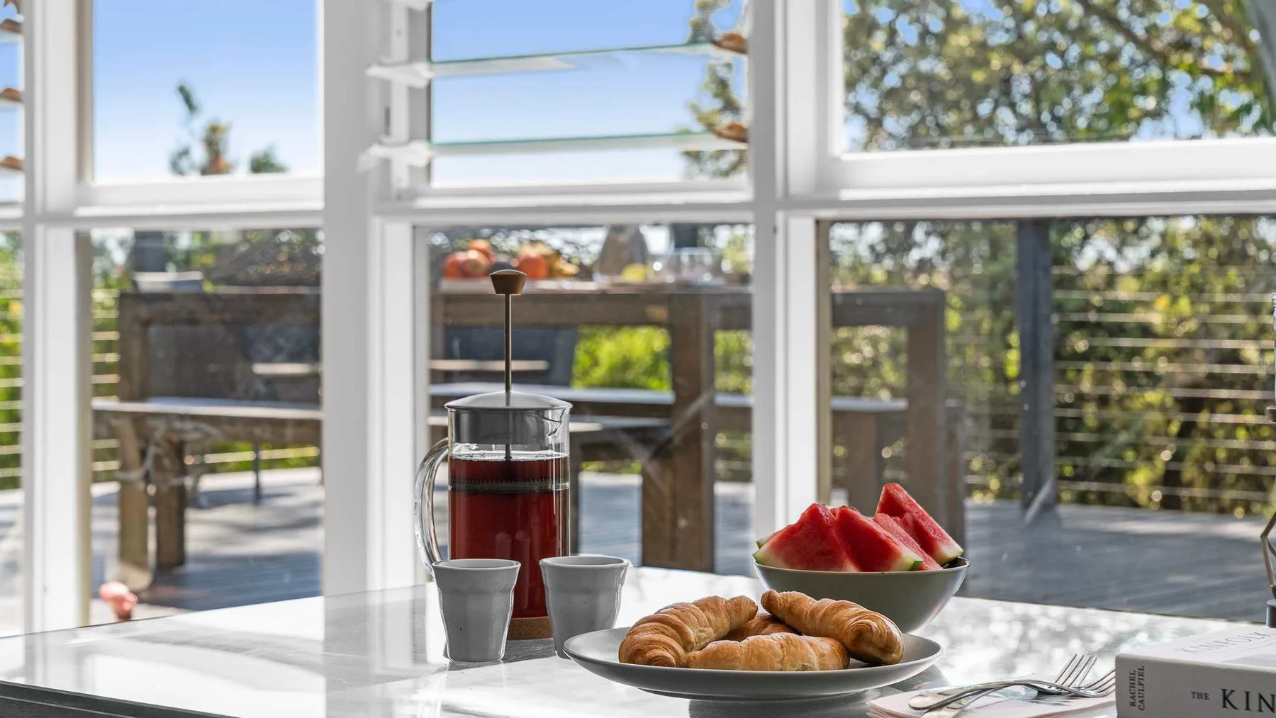 Un desayuno con bollería y fruta junto a ventanas con vistas a una terraza.