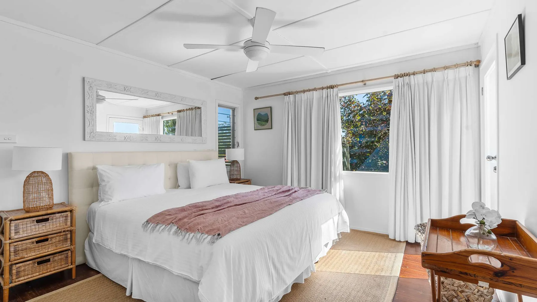 Un dormitorio luminoso con una cama grande y cortinas blancas junto a una ventana.