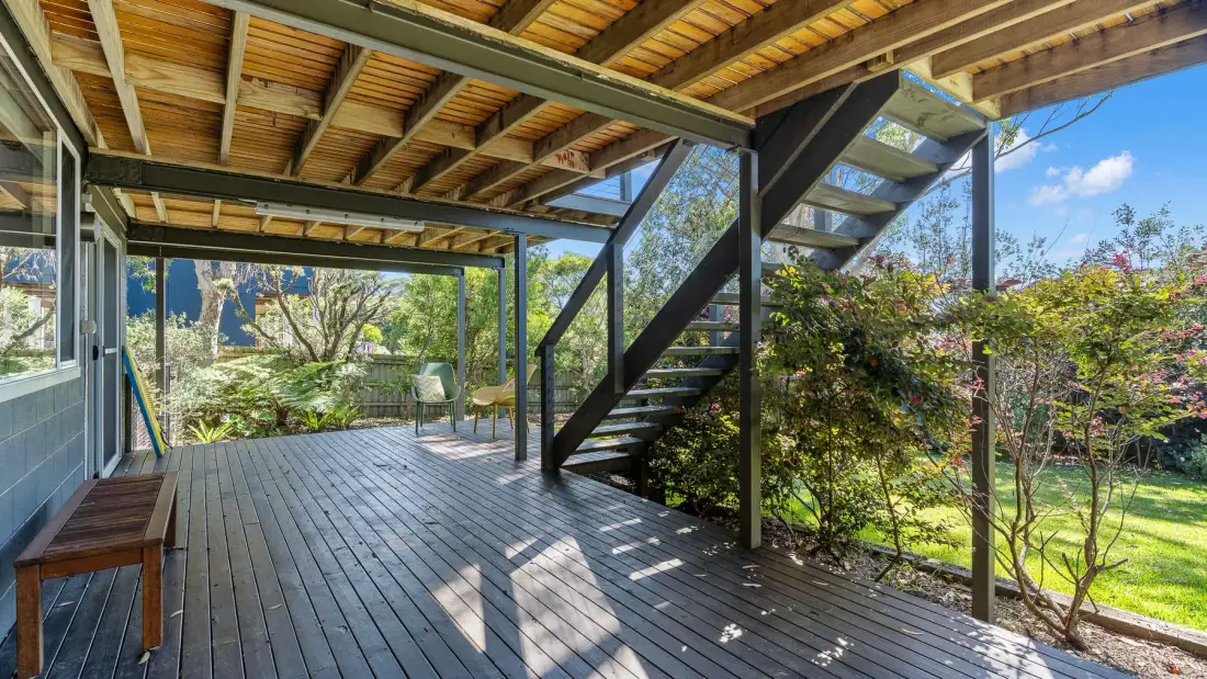 Una terraza exterior cubierta con escaleras y vistas al jardín.