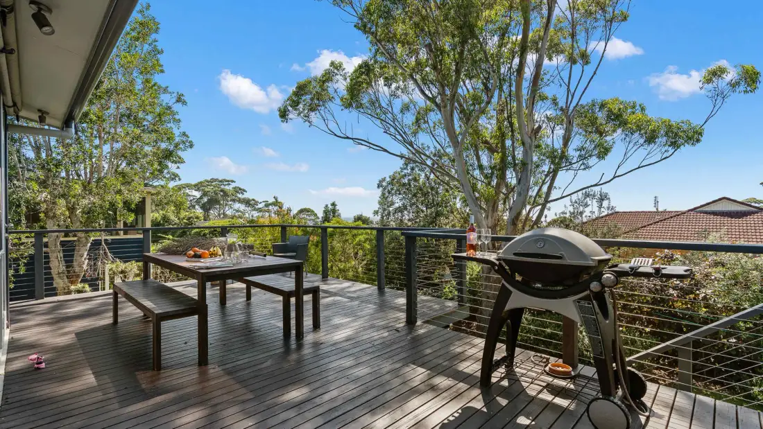 Una terraza exterior tiene una mesa de comedor y una barbacoa junto a la barandilla.