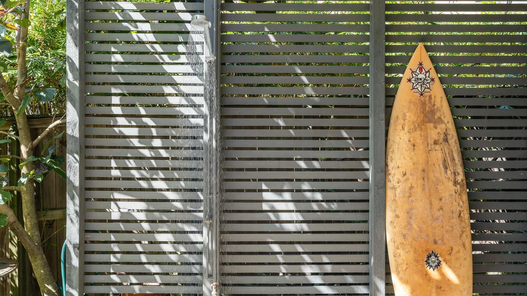 Un espacio exterior con una tabla de surf de madera apoyada en una valla de listones.