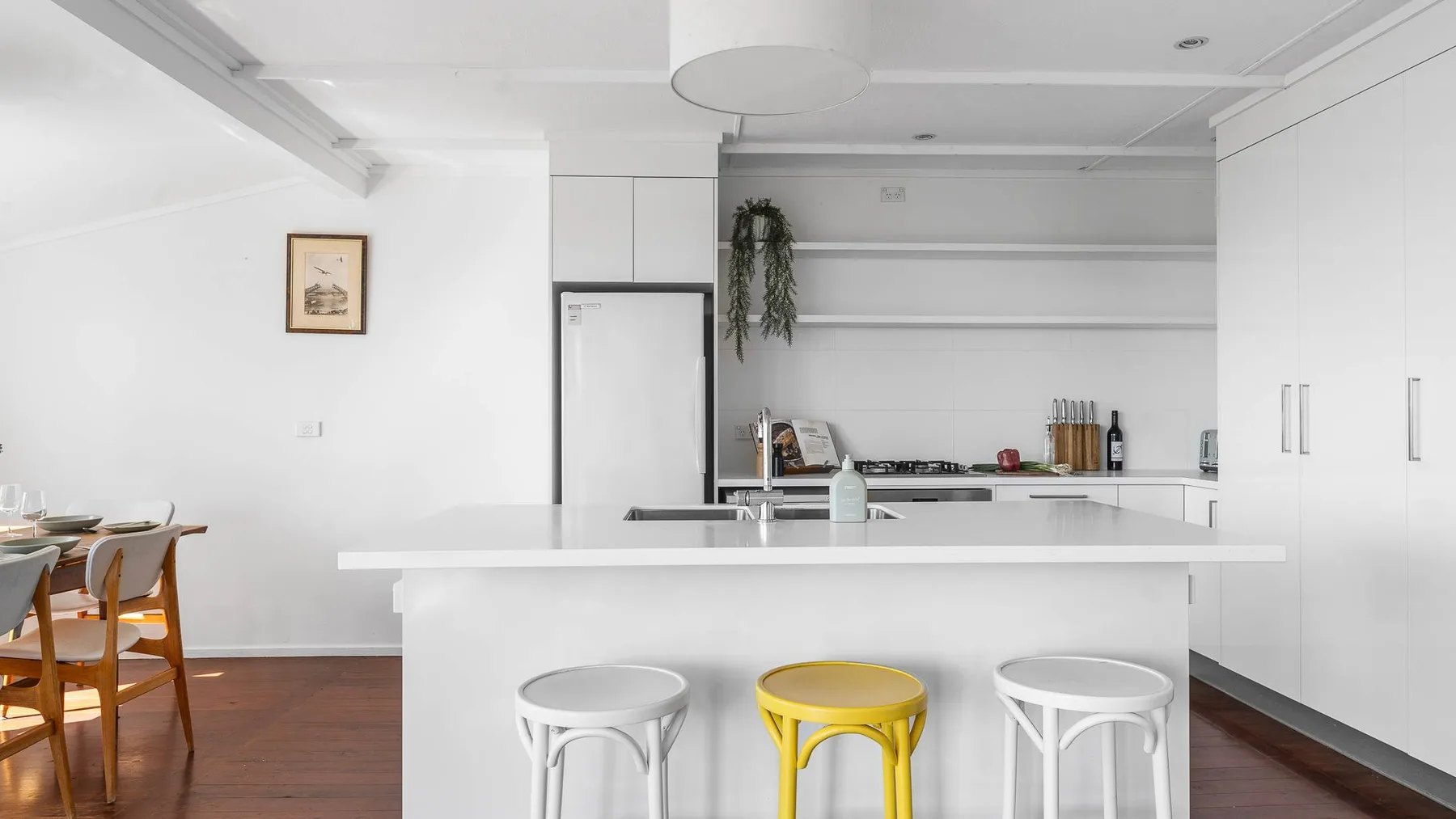 Una cocina blanca y luminosa con una isla y tres taburetes.