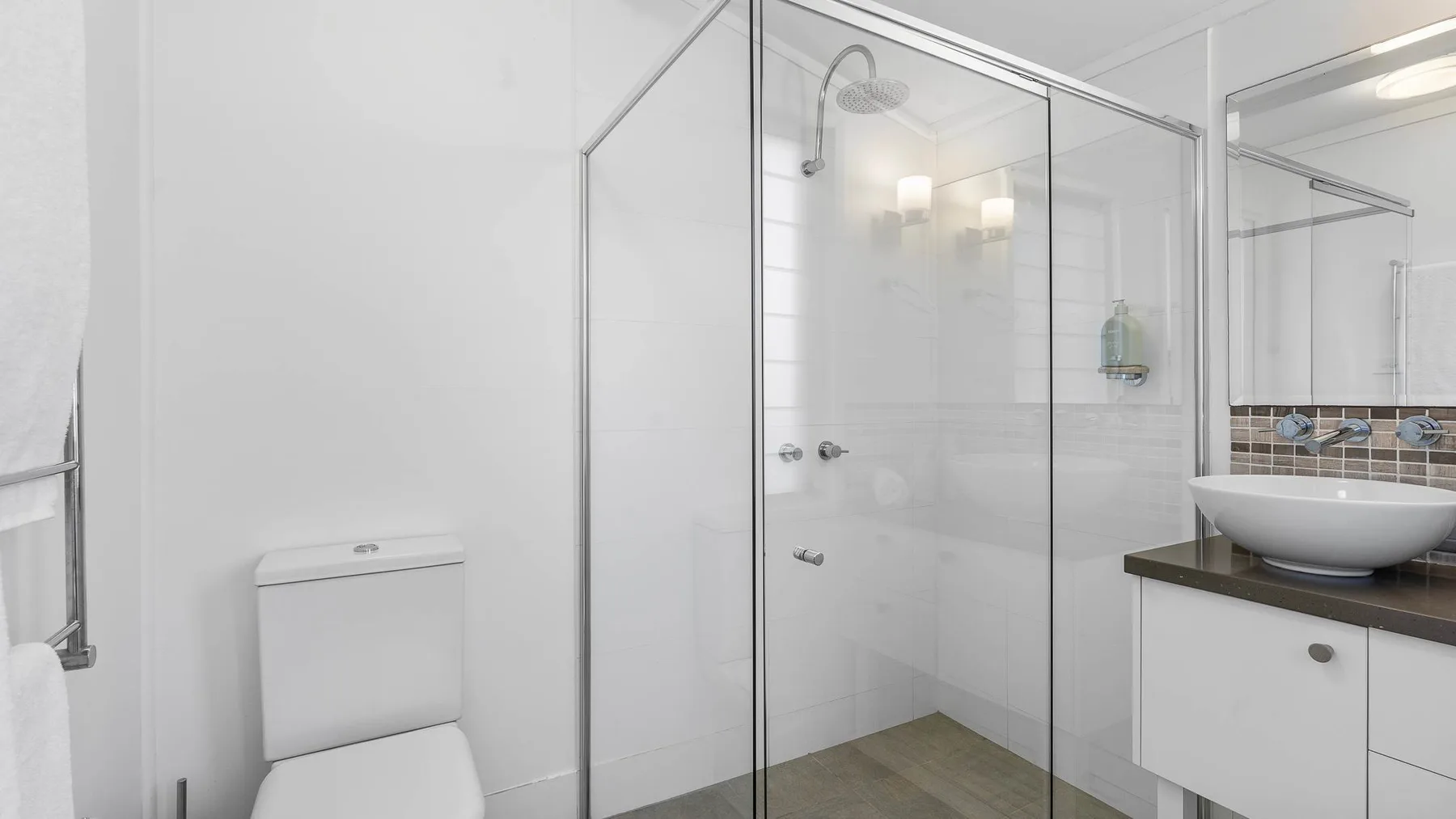 Un baño luminoso con una ducha de vidrio y un lavabo sobre el tocador.
