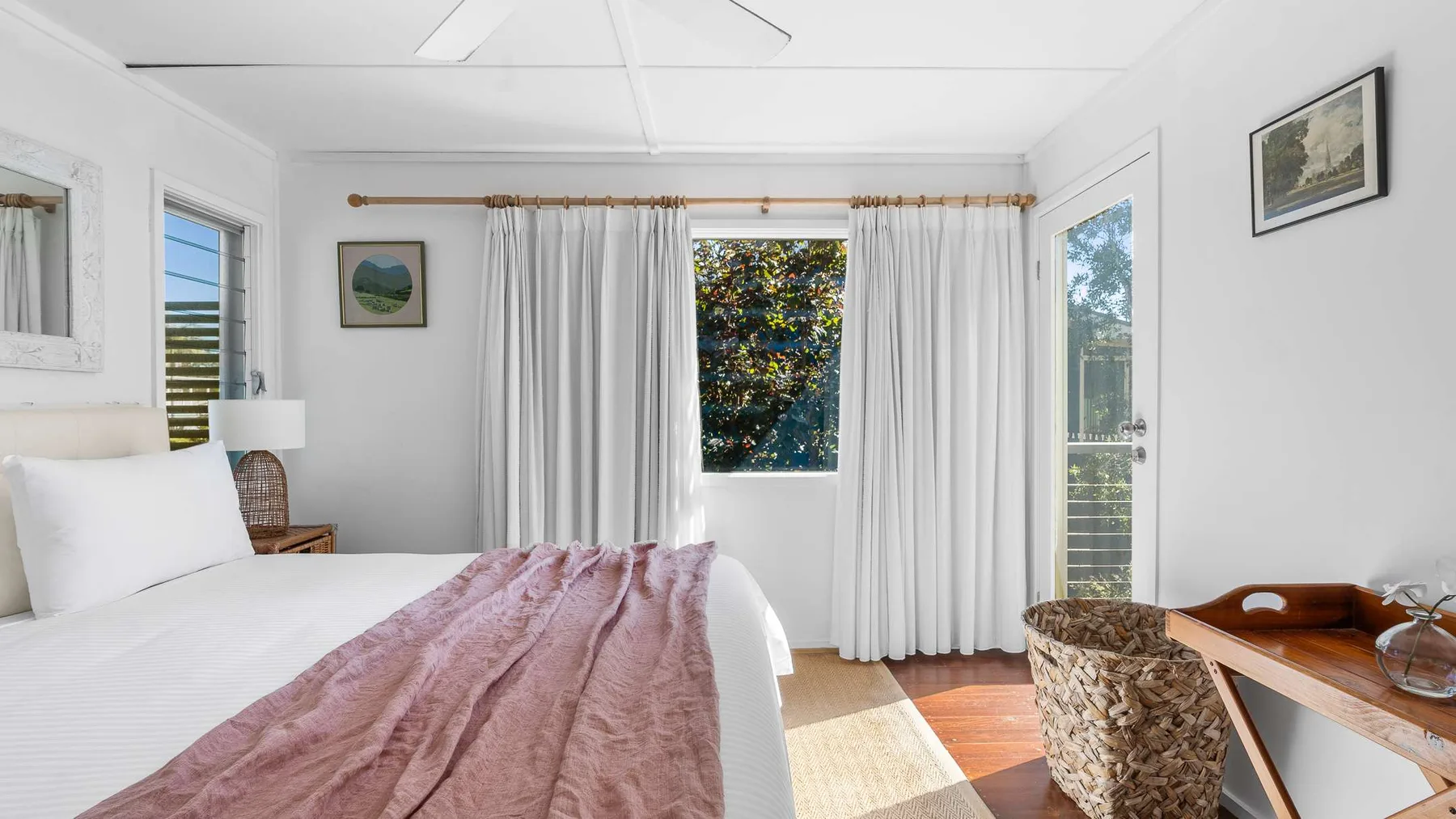 Un dormitorio luminoso con cortinas blancas, una cama y un escritorio pequeño.