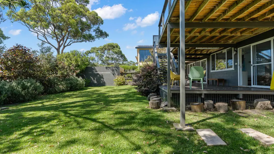 Un patio con césped junto a una zona cubierta para sentarse y un jardín.