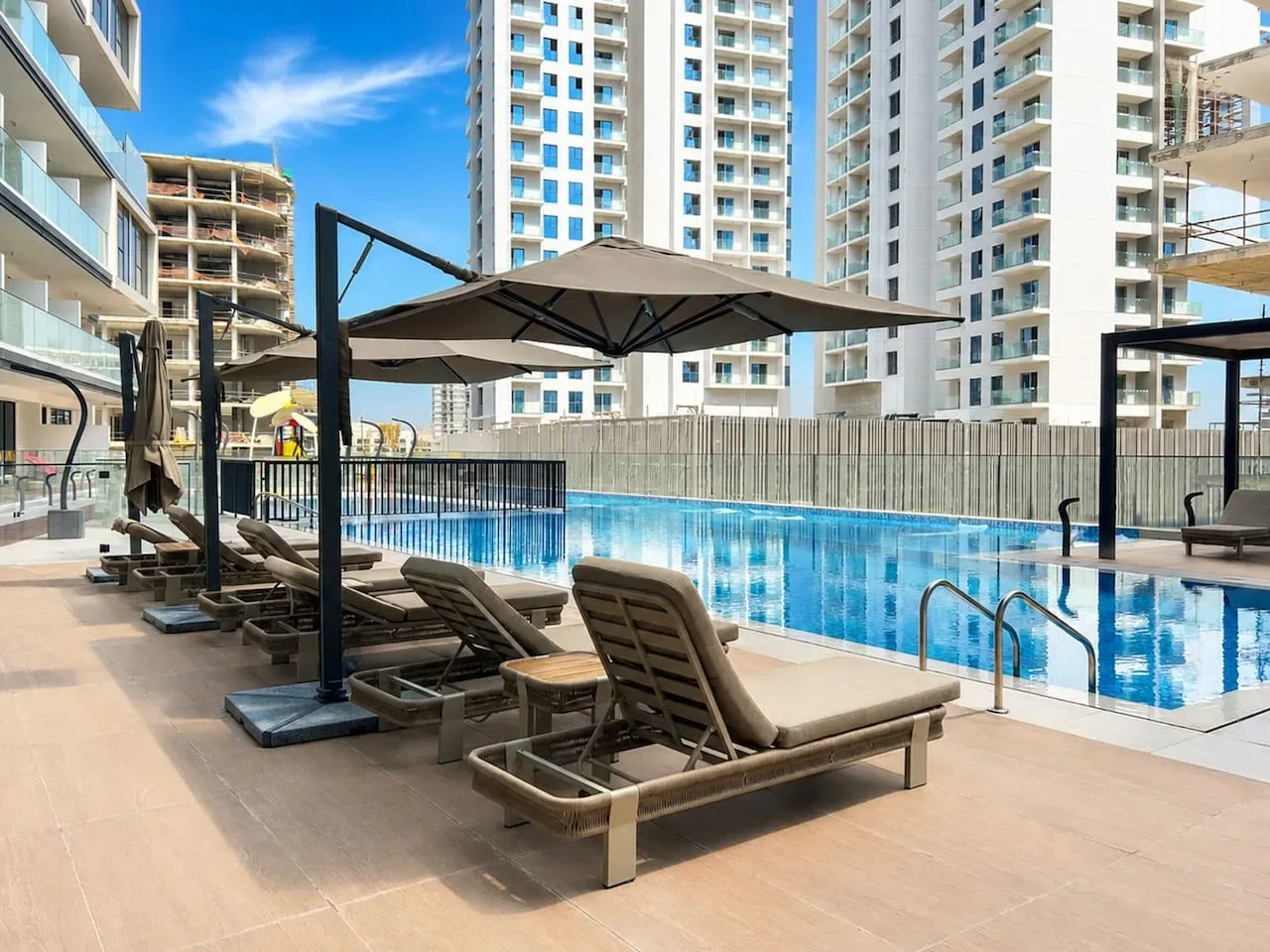 Una zona de piscina al aire libre con asientos reclinables y una sombrilla grande.