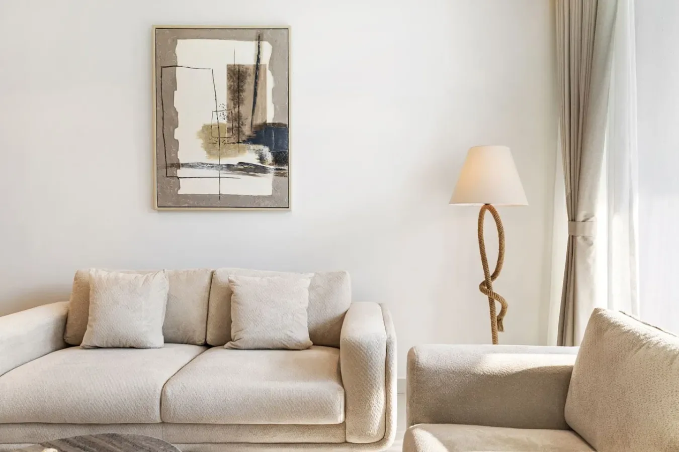 Una sala luminosa con asientos claros, una obra enmarcada y una lámpara de pie.