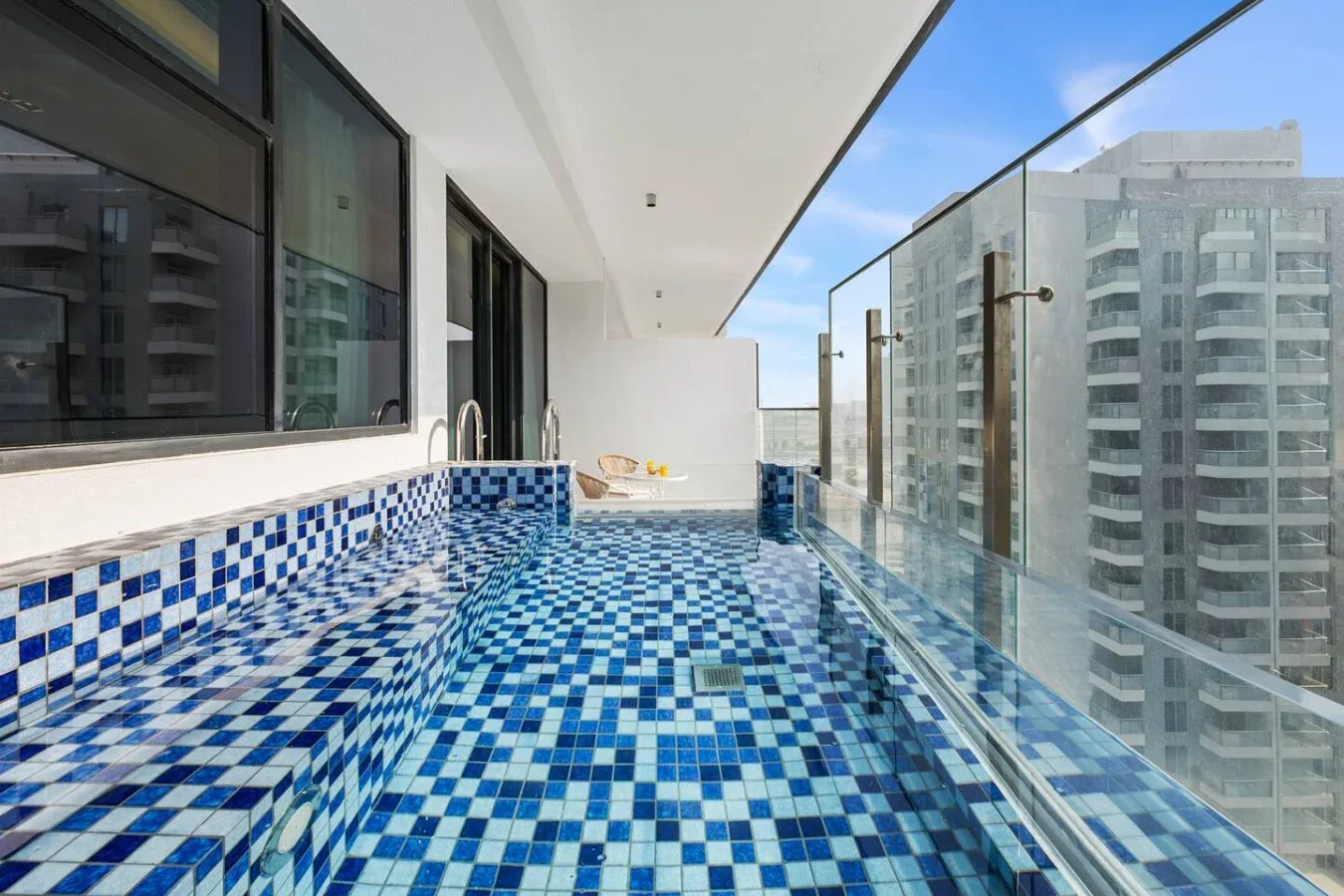 Una estrecha piscina exterior de azulejos bordea barandillas de vidrio y grandes ventanas.