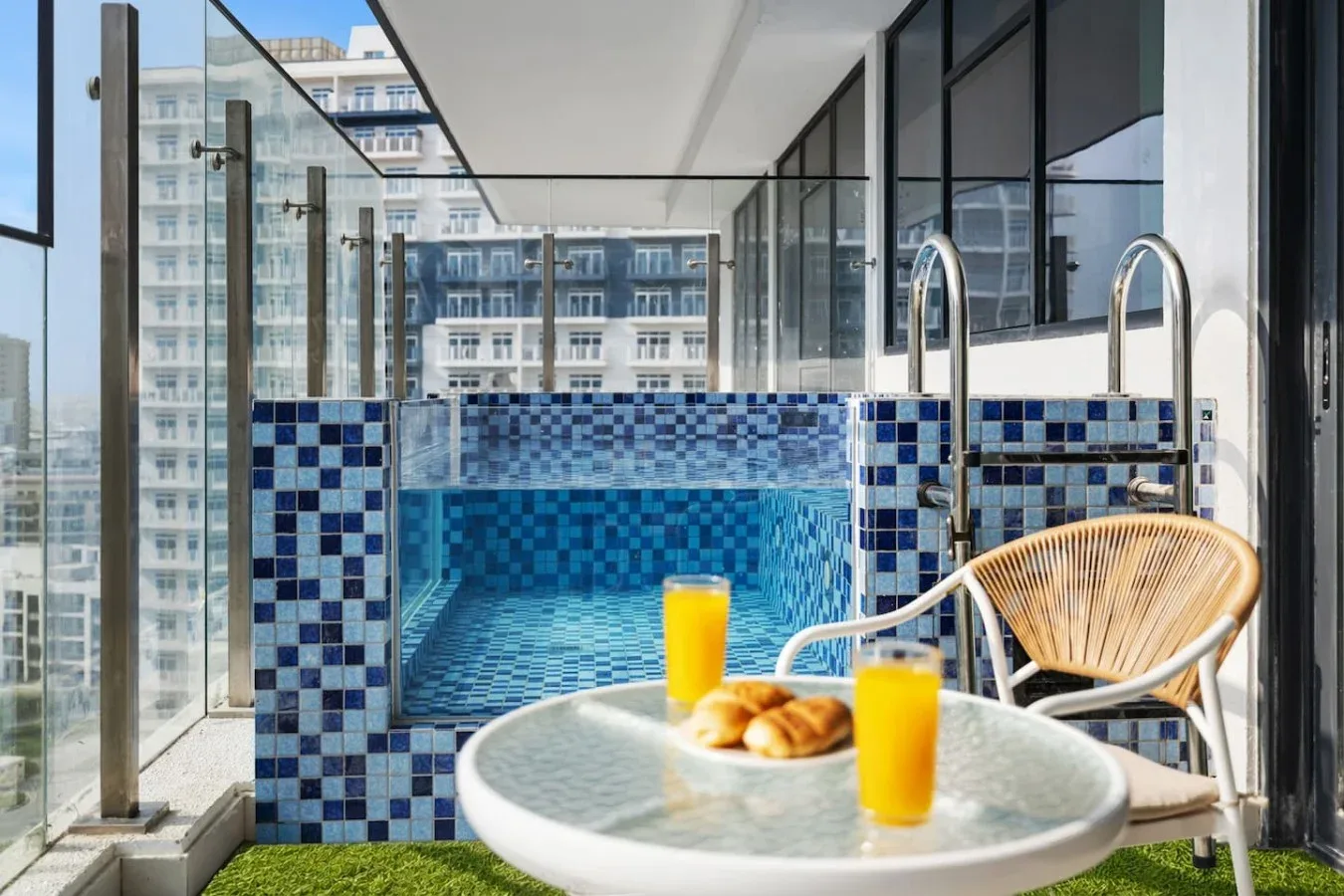 Una pequeña piscina de azulejos junto a una mesa redonda con bebidas y bollería.